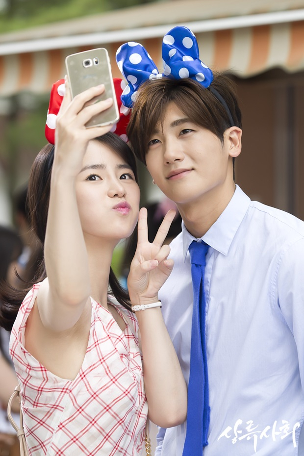 This scene from the drama, "High Society," shows a couple with matching hairbands taking photos during a date in an amusement park (SBS)