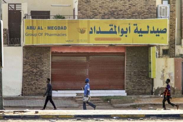 Men walk past a closed pharmacy in the south of Khartoum on April 17, 2023 as fighting in the Sudanese capital between the army and paramilitary forces led by rival generals rages for a third day. (Photo by AFP)