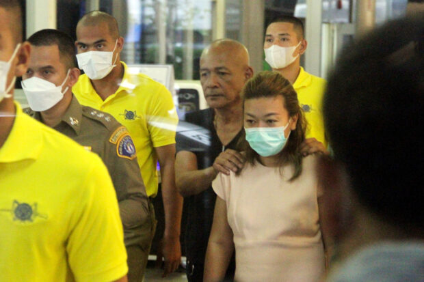 Sararat Rangsiwuthaporn, a suspect in over a dozen murders, is escorted by police officers at a police station in Bangkok
