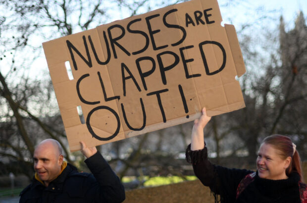 Healthcare workers hold placards at a picket line outside St Thomas' Hospital in London on February 6, 2023 as the UK faced the biggest round of health service strikes. - Nurses and ambulances staff stepped up their demands for better pay to combat the UK's cost of living crisis. The stoppages -- part of a wave of industrial action across the UK economy -- will see nurses and paramedics take action on the same day for the first time. (Photo by Daniel LEAL / AFP)
