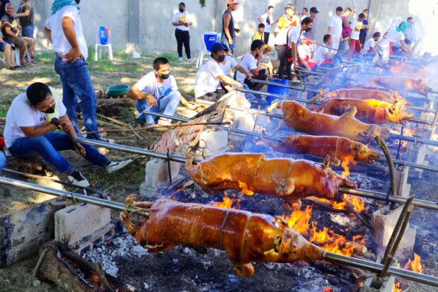 "Lechoneros," the men and women who roast pigs for a living, from the village of Lasip Chico in Dagupan City put pigs over fire, continuously turning the metal pole until they turn brown at the first "Lechonan ed Barangay" on Saturday, May 6, 2023. STORY: 14 roasted pigs sold in single day in Dagupan's rising ‘lechon capital’