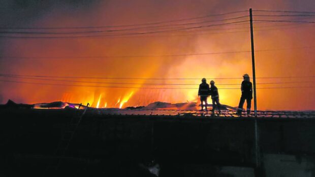 CALLED TO DUTY   From the roof of a building adjacent to burning warehouses, firefighters try to extinguish the blaze that destroyed three structures in Porac town, Pampanga province, on Monday. At least P4 billion worth of cigarettes, raw materials and manufacturing machines seized by the government in its crackdown of counterfeit products were lost to the fire. —JUN A. MALIG