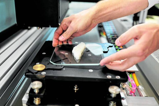 A worker removes a piece of cultivated grouper fish from a 3D printer at Steakholder Foods in Rehovot, Israel, in this photo taken on April 23, 2023. STORY: 3D printers spawn new kind of fish to fry