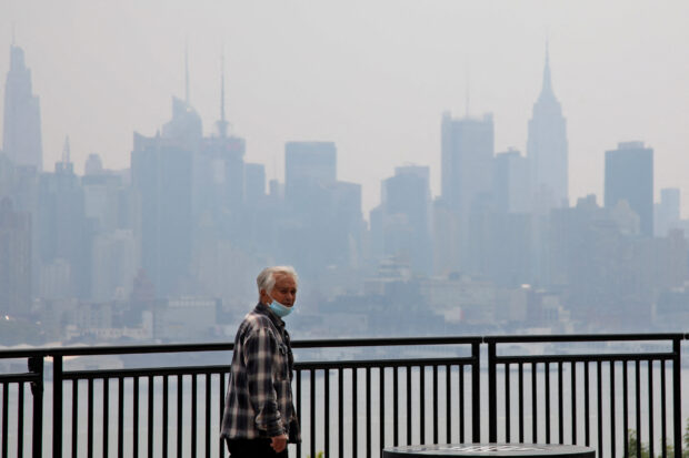 The Manhattan skyline is seen across the Hudson river past a pedestrian walking along the waterfront in West New York, New Jersey, on June 8, 2023, as smoke haze from Canadian wildfires blankets the area. Smoke from Canadian wildfires continued to shroud US cities in a noxious haze Thursday, forcing flight delays and cancellations to outdoor activities as environmental groups called for urgent action to tackle climate change. (Photo by Leonardo Munoz / AFP)