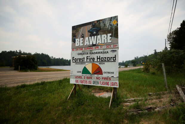 A fire hazard sign sits beside a highway near a forest fire that has been burnin