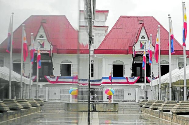 Amid the rainy weather, a woman visits the Aguinaldo Shrine on the eve of Independence Day, its facade also reflected on the pedestal of President Emilio Aguinaldo’s statue fronting his home. STORY: The row, rebrandings behind Independence Day