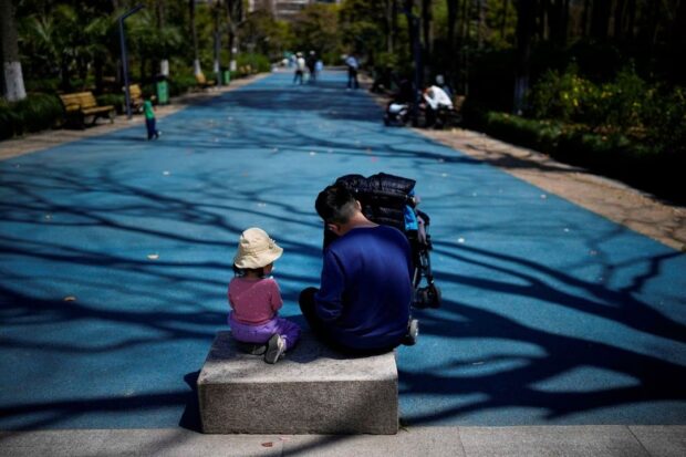 A little girl sits with her dad in a park in Shanghai, China, April 2, 2023. REUTERS/Aly Song/File Photo chinese pay kids