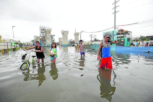 MORE FLOODS Residents in Marilao town in Bulacan province wade through its flooded streets near pillars for the overhead MRT 7 rail line on Saturday. The weather bureau warns of more rains in the coming days from Tropical Storm “Falcon” (international name: Khanun), which is now east of Luzon over the Philippine Sea. —LYN RILLON