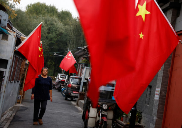 FILE PHOTO: A woman walks through a hutong alley hung with Chinese national flags, ahead of the 20th National Congress of the Communist Party of China, in Beijing, China October 14, 2022. REUTERS/Tingshu Wang/File Photo