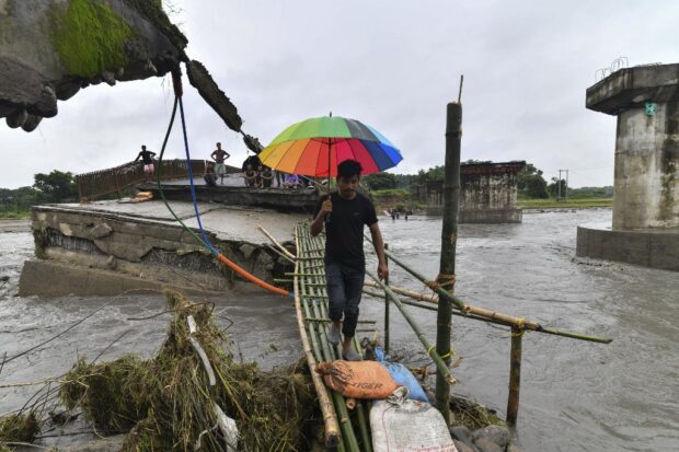 A man walks across a makeshift bamboo bridge after a section of a bridge over the Daranga River washed away after flash floods following monsoon rains in Kumarikata village of Baska district, some 52 Km from Guwahati in India's Assam state on June 23, 2023. At least 19 people are dead after floods triggered by South Asia's annual monsoon, with a week of relentless rains forcing thousands of people to seek shelter in India. (Photo by Biju BORO / AFP)