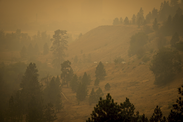 Smoke from wildfires fills the air as motorists travel on a road on the side of a mountain, in Kelowna, British Columbia, Saturday, Aug. 19, 2023. 