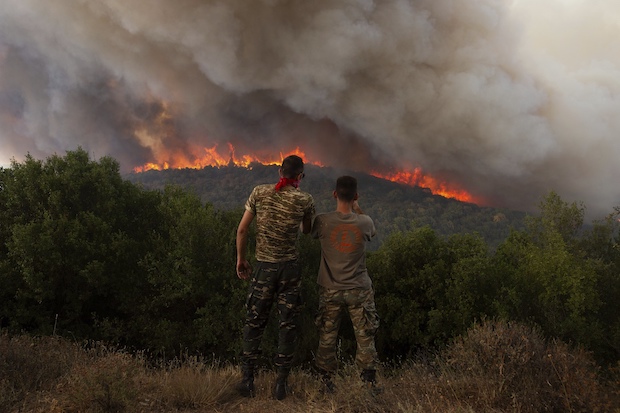 Two men on a hill watching a wildfire in Greece