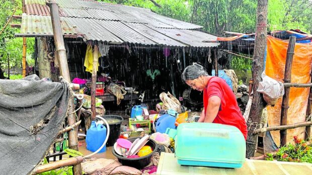 BACK ON THEIR FEET Nora Sarmiento, 51, a resident of San Antonio, Zambales, ignores the rain as she starts cleaning the family’s flood-soaked belongings on Tuesday. Her village of San Miguel was hit by heavy flooding when Typhoon “Egay” (Doksuri) battered central and northern Luzon early this week. —JOANNA ROSE AGLIBOT