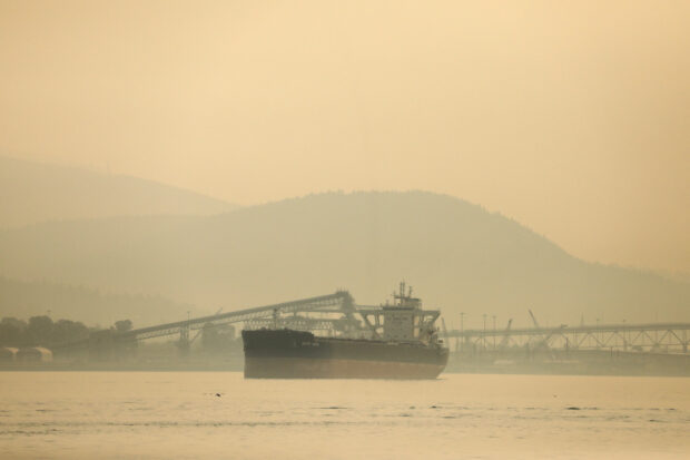 A bulk carrier lies at anchor in Vancouver Harbour, shrouded in a haze a wildfire smoke