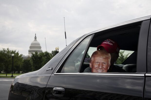  a supporter of former U.S. President Donald Trump holds up a cutout of Trump as rides in a car