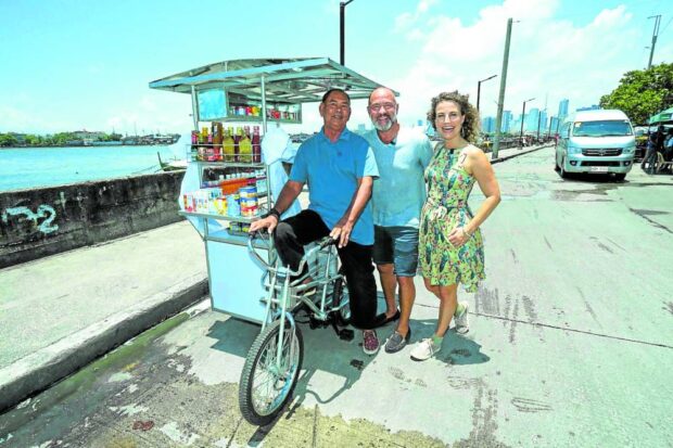 Reynaldo Balingit (left) is shown at thepedal of the fishball cart donated by David Katz (middle) and his chief relations officer Taylor Leigh Cannizzaro.