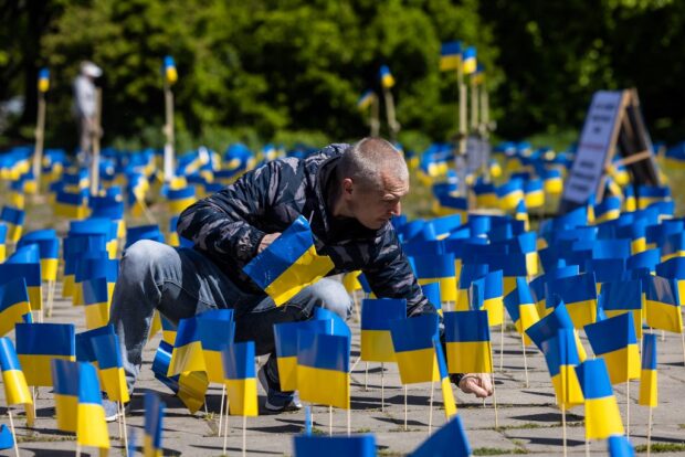 A man sticks a flag beside other Ukrainian flags and crosses with the names of victims, during a protest organized by activists of the Ukrainian diaspora at the Soviet soldier war mausoleum in Warsaw, on May 9, 2023, the 78th anniversary of the victory over Nazism and the end of the World War II in Europe. (Photo by Wojtek Radwanski / AFP)