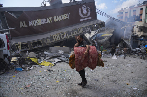Palestinians walk by the destroyed building of Al Nuseirat Bakery in an Israeli airstrike 