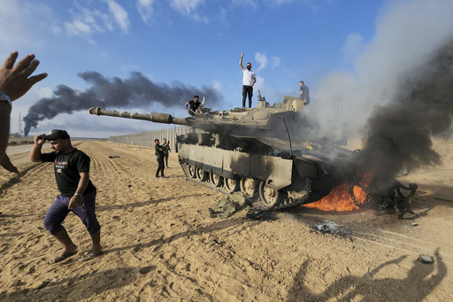 Palestinians celebrate by a destroyed Israeli tank at the border fence between Israel and the Gaza Strip, east of Khan Younis, during a surprise attack on Israel, Saturday, Oct. 7, 2023.