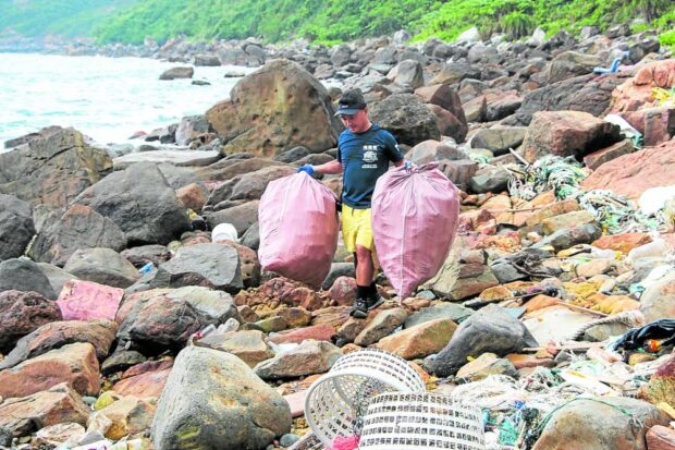 NOT JUST MANILA BAY This picture taken on Nov. 9 shows a man carrying bags filled with plastic waste during a beach-cleaning drive near Clear Water Bay in Hong Kong. —AFP