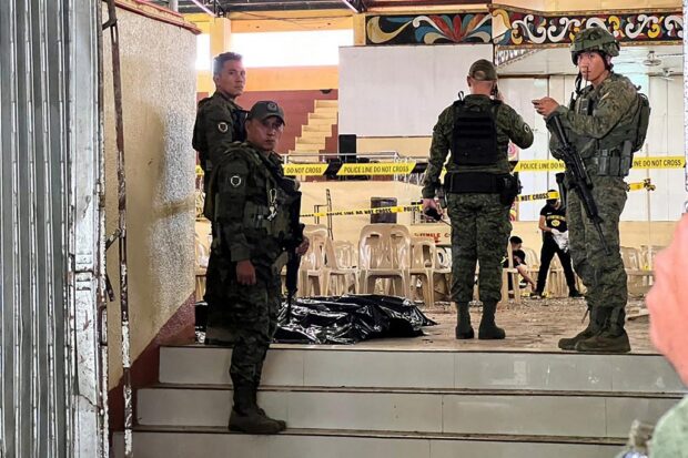 Military personnel stand guard at the entrance of a gymnasium while police investigators (background) look for evidence after a bomb attack at Mindanao State University in Marawi, Lanao del Sur province on December 3, 2023. 