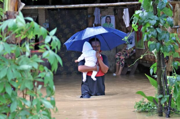 IN FATHER’S ARMS A father holds his child tight as they cross the rising floodwater in Barangay Patin-ay, Prosperidad, Agusan del Sur, at the height of Tropical Storm “Kabayan” on Monday. —ERWIN MASCARIÑAS