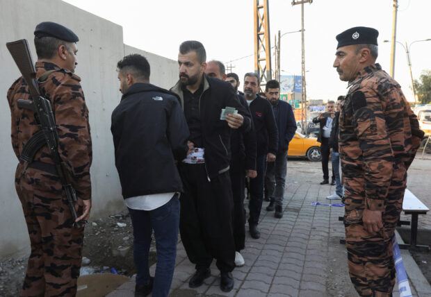 People stand in line to undergo security checks before gaining entry to a polling station to vote for Iraq's provincial council elections, in Kirkuk