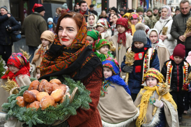 A woman walks through the streets carrying traditional doughnuts as she takes part in Christmas Eve celebration in Lviv, on December 24, 2023, amid the Russian invasion of Ukraine. Ukrainians attend Christmas Eve services as they prepare to celebrate Christmas Day on December 25 for the first time, after the government changed the date from the Orthodox Church observance of January 7 in a snub to Russia, on December 24, 2023. (Photo by YURIY DYACHYSHYN / AFP)