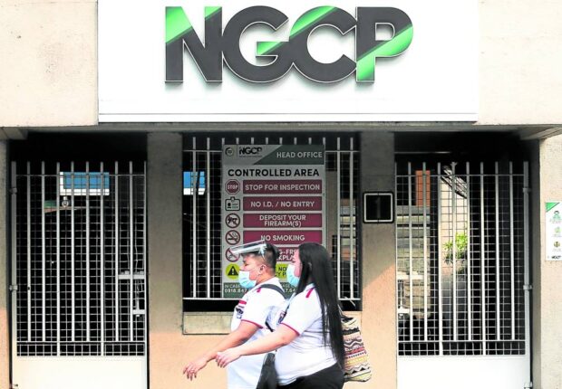 Pedestrians walking past a building with the NGCP logo