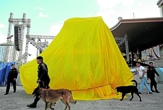 NEW RIDE Policemen with bomb-sniffing dogs inspect the still covered “andas” (carriage) of the Black Nazarene at Quirino Grandstand in Manila on Monday. The new carriage, featuring a tempered glass enclosure and equipped with security camera, will be unveiled in today’s procession. —RICHARD A. REYES