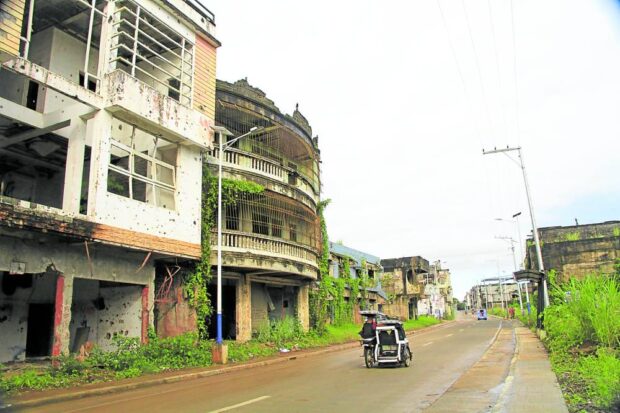 CONTRAST Damaged structures provide a stark contrast tothe newly paved road, restored electricity lines and newly installed solar-powered street lights in Marawi City, in this May 2022 photo. —RICHEL V. UMEL