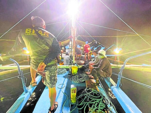 Personnel from the Bureau of Fisheriesand Aquatic Resources (BFAR) in Quezon province board a commercial fishing boat cited for illegal fishing in Lamon Bay off Calauag town in this photo taken on April 26, 2022.