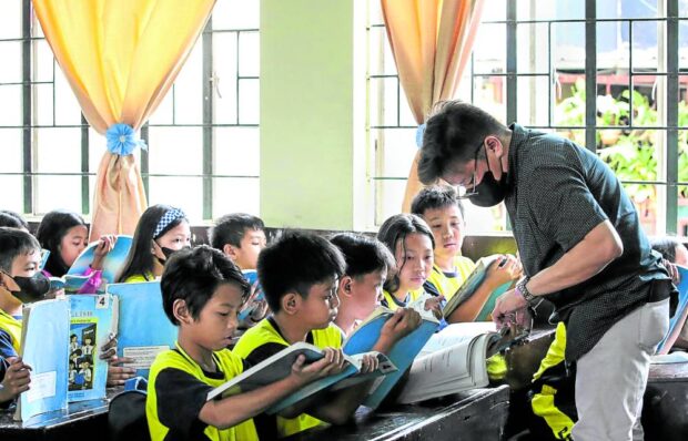 DEFINING DEDICATION Teacher Edito Ansale Jr. helps out pupils during a reading drill at Corazon Aquino Elementary School in Quezon City. —LYN RILLON