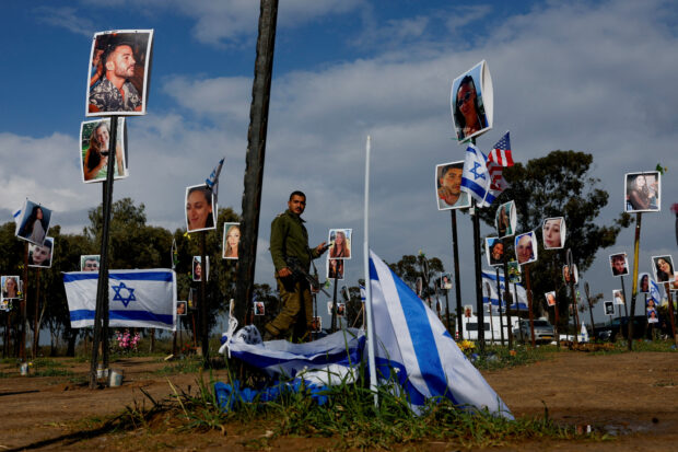 Israeli soldier walks near pictures that are part of an installation at the site of the Nova festival, in Reim