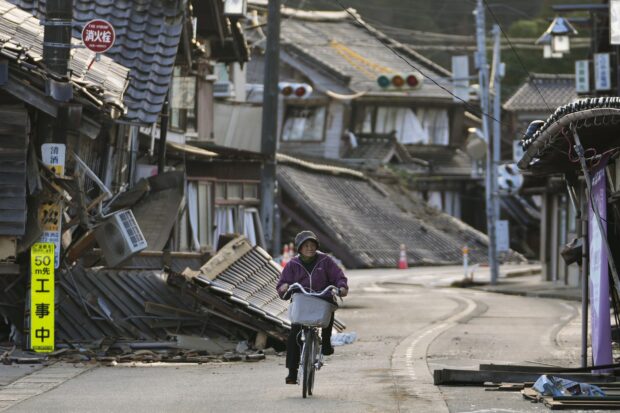 A woman bikes amid damaged houses in Noto town in the Noto peninsula facing the Sea of Japan, northwest of Tokyo, Tuesday, Jan. 2, 2024, following Monday’s deadly earthquake. A series of powerful earthquakes that hit western Japan have damaged thousands of buildings, vehicles, and boats. Officials warned that more quakes could lie ahead. 