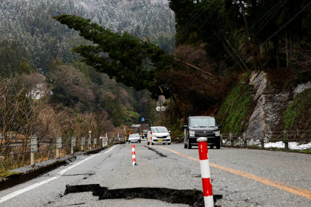 Cars drive past a damaged road, in the aftermath of an earthquake, in Wajima, Ishikawa Prefecture, Japan, January 7, 2024.