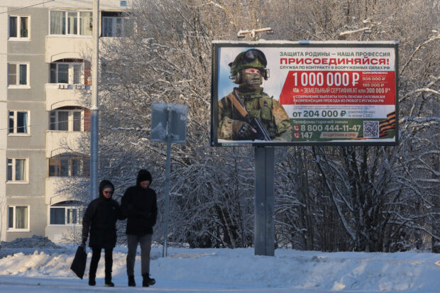 People walk along a street past a billboard promoting military service under the contract in Russian Armed Forces in the town of Gatchina