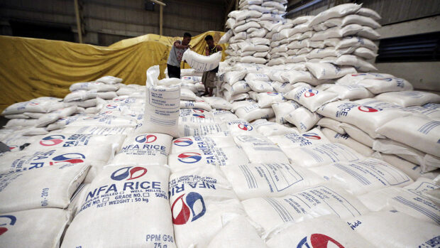 PHOTO: Workers on top of sacks of rice at an NFA warehouse. STORY: Acting NFA chief also gets suspended over rice deal
