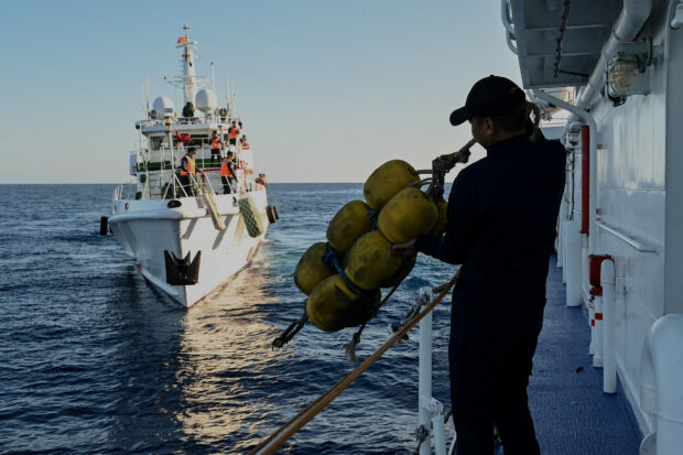 PHOTO:  Philippine Coast Guard crew member, holding a rubber fender, watches as a China Coast Guard vessel sails near the BRP Sindangan during a supply mission to Ayungin (Second Thomas) Shoal in the West Philippine Sea, on Tuesday, March 5, 2024. STORY: Damaged PH vessel was on ‘test mission,’ not loaded