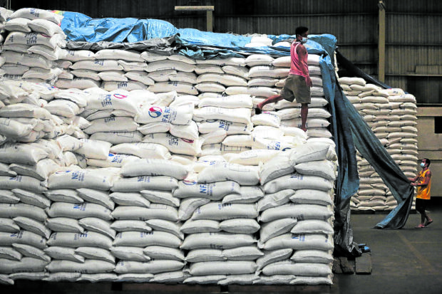 PHOTO: Worker on top of sacks of NFA rice in a warehouse STORY: House inquiry raises more issues in NFA rice sale