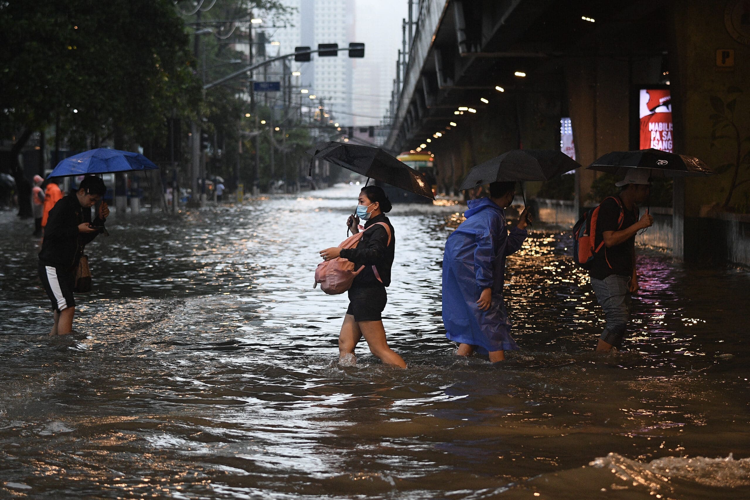Pedestrians cross a flooded street in Manila on July 24, 2024 amid heavy rains brought by Typhoon Carina. Relentless rain drenched the northern Philippines on July 24, triggering flooding in Manila and landslides in mountainous regions as the typhoon intensified the seasonal monsoon. (Ted ALJIBE / AFP)