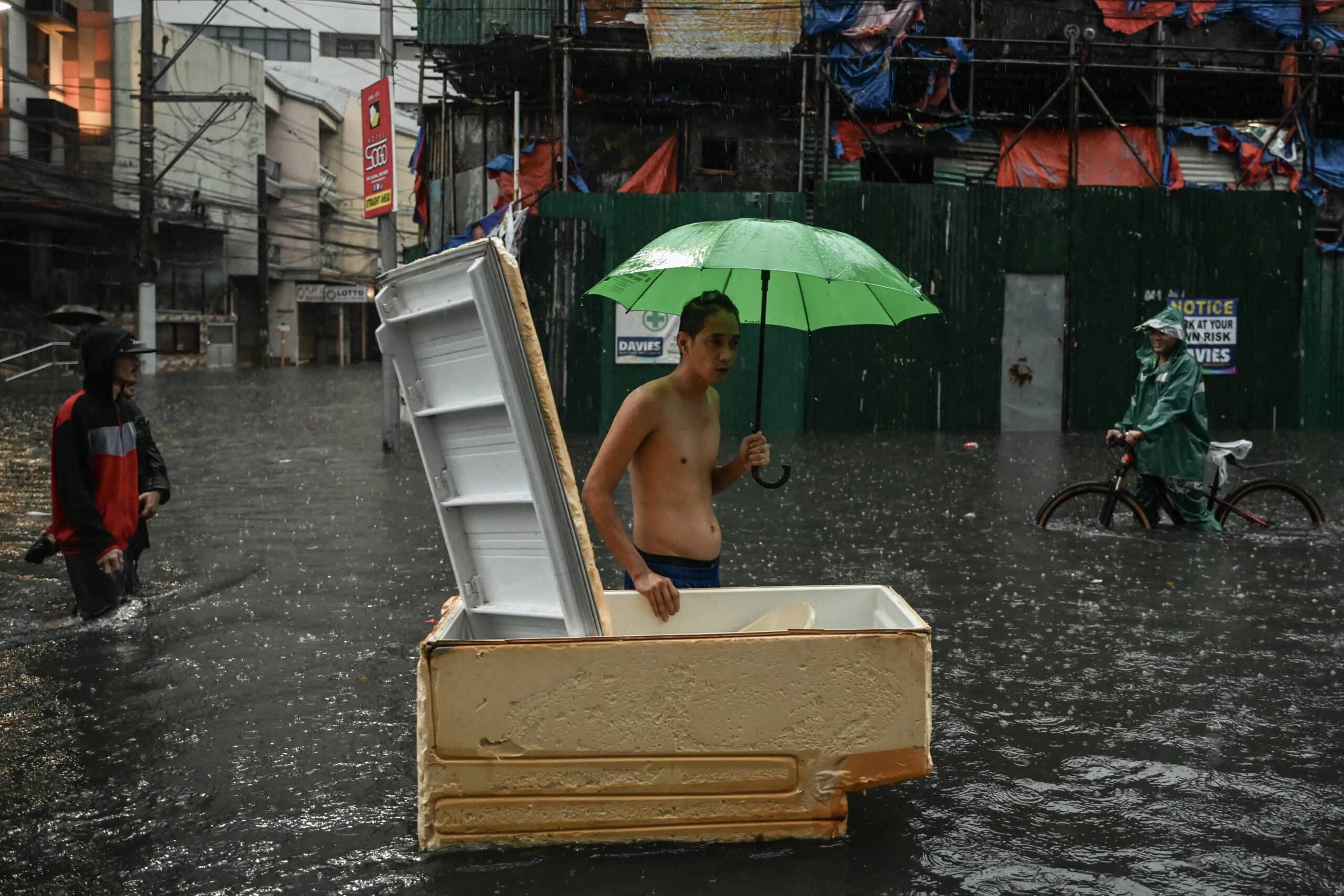 People walk along a flooded street in Manila on July 24, 2024 amid heavy rains brought by Typhoon Gaemi