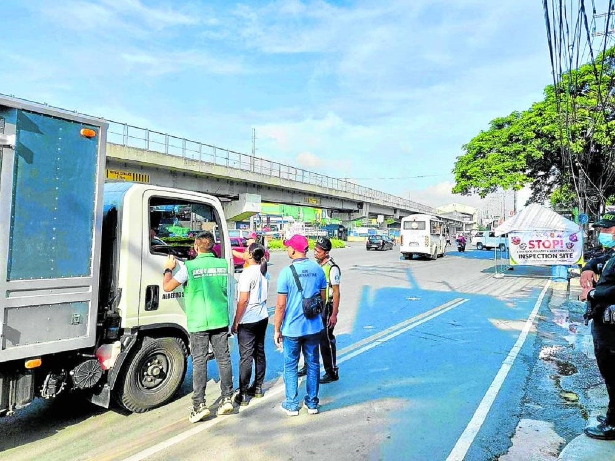  In this photo taken last week, Bureau of AnimalIndustry (BAI) personnel manning a checkpoint flag down a delivery truck for inspection along a road in Quezon City as the agency intensifies measures to prevent the spread of African swine fever.