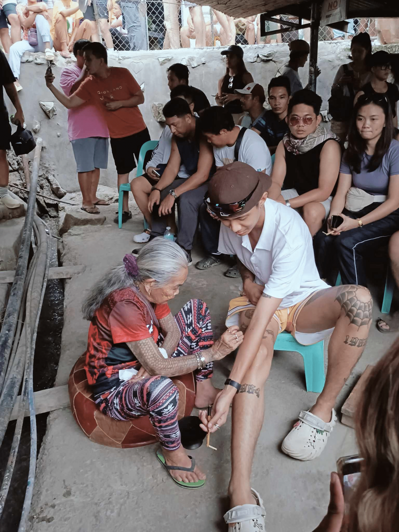 Tourists flock to Buscalan tattoo village to meet famous "mambabatok" Apo Whang-Od on Saturday, August 24, 2024. While she is still unable to do tattoo work, she is seen in the photo using her free hand holding a stencil to put an ink on a tourist's arm. (Photo from Anna Tambalong)