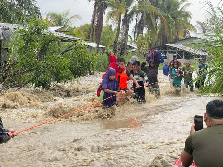 Local government disaster workers of Northern Kabuntalan, Maguindanao del Norte help trapped civilians cross a flooded road following heavy down pour that triggered floods. (Photo from N. Kabutnalan MDRRMO)