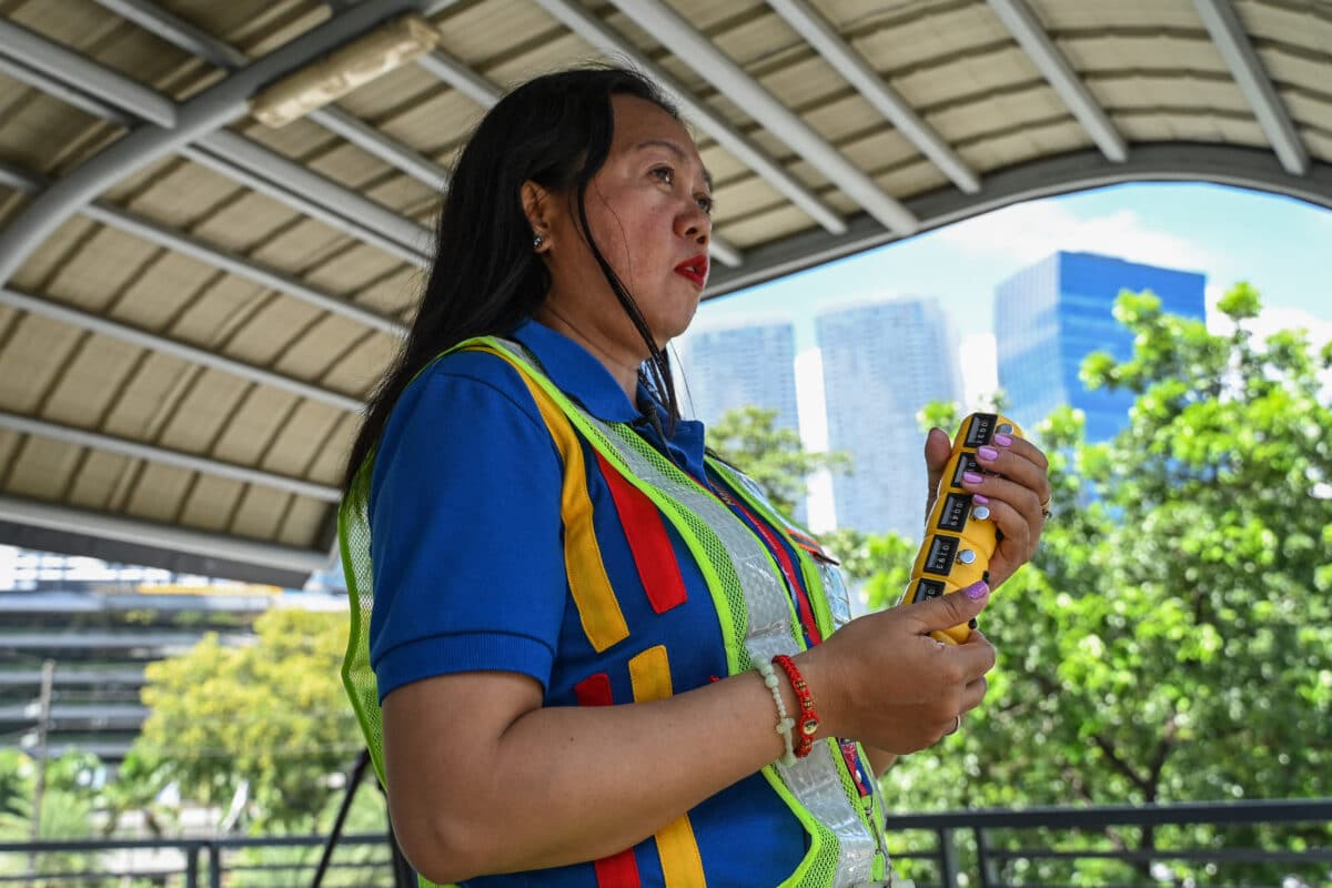 This photo taken on August 22, 2024 shows traffic surveyor Irna Lapriza manually counting passing vehicles from a footbridge in Pasig City, Metro Manila. - Rain or shine, through floods and car exhaust pollution, some 34 traffic surveyors employed by the city government are deployed to at least 16 major roads in the Philippine capital - their eyes jumping from one car to the next, fingers clicking manual tally counters as they log each passing vehicle. Their tallies end up with the traffic engineers of the Metropolitan Manila Development Authority (MMDA), who design and propose inexpensive traffic solutions. (Photo by Jam Sta Rosa / AFP)