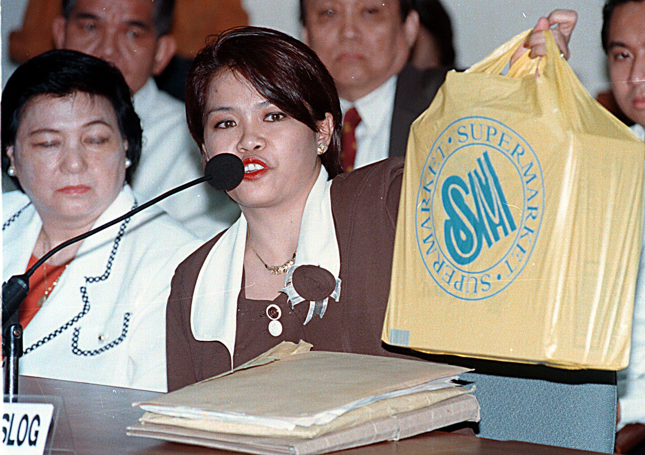 BAGWOMAN Mary Ann Maslog, photographed here onMarch 9, 1999, appears before a congressional hearing where she shows the plastic bag of mugs supposedly intended as gifts for Malacañang officials. Unfortunately, Maslog claims, she brought the wrong bag to the Palace—one containing P3 million in cash. 