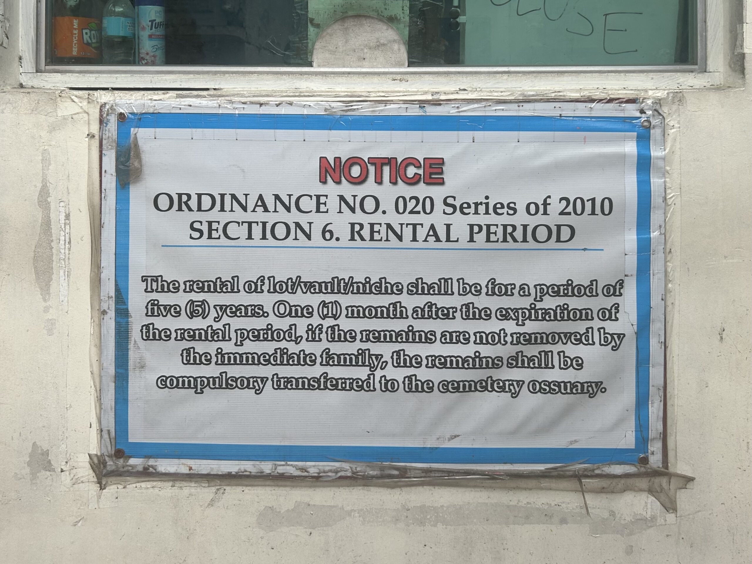 Poster Pasal 6 Peraturan Daerah Kota Marikina Nomor 020 Seri Tahun 2010 terpampang di depan kantor tata usaha pemakaman. 