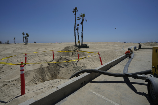 Seal Beach resident Tom Ostrom, right, sits along an empty water-pipe to be used to pump sea water back to the Pacific Ocean as homes are protected by sand berms in Seal Beach, Calif., Friday, Aug. 18, 2023. 